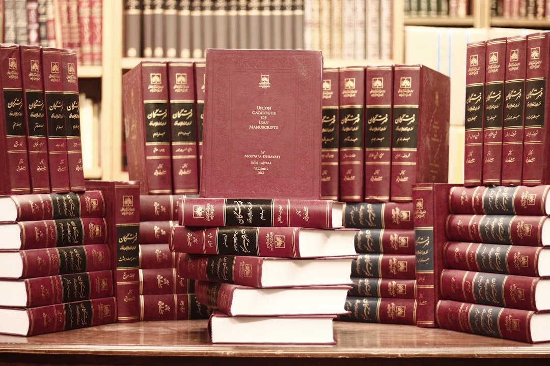 Photo by Benyamin Bohlouli a stack of red books sitting on top of a wooden table